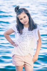 Portrait of little fashionable girl walking on berth near sea