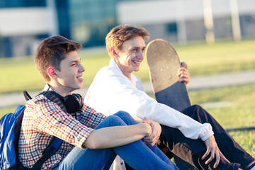 Two teenagers in a good mood with a skateboard rest in the park at sunset of the day © Vyacheslav Kharkin