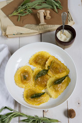 Grilled vegetables ravioli with sage butter. White wooden table, white plate.