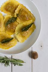 Grilled vegetables ravioli with sage butter. White wooden table, white plate.