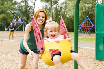 Fototapeta na wymiar Mother and daughter in a swing having fun at the park playground