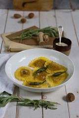 Grilled vegetables ravioli with sage butter. White wooden table, white plate.
