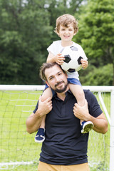 Young father with his little son playing football on football pitch