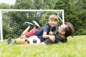 Fototapeta premium Young father with his little son playing football on football pitch