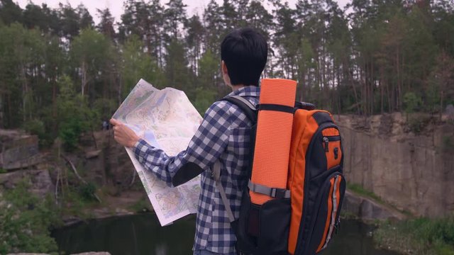 Woman hiker standing in canyon holding map looking the road. Brunette backpacker rear back view with backpack in spring season.