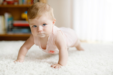 Little funny baby girl lifting body and learning to crawl.