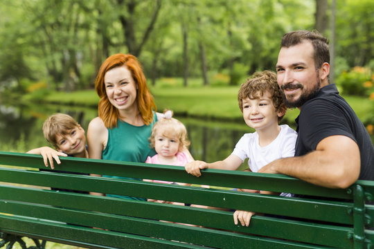 Happy Family Sitting On Bench In Park