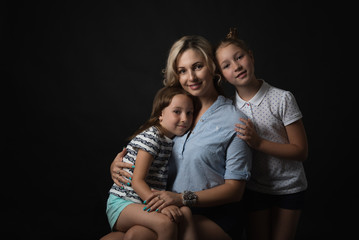 Cute family portrait of mother hugging with daughters on black studio background