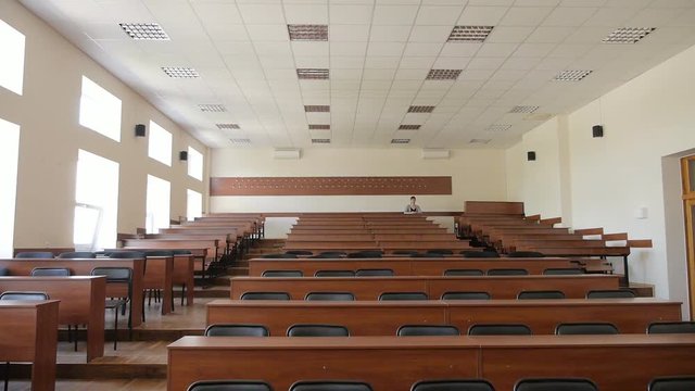 View of empty lecture hall, in the back row sits a girl student
