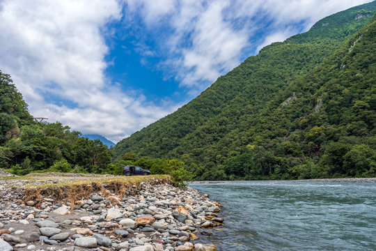 Road trip by car. A car standing near the river on a pebble rocks in the mountains. Wild nature background.