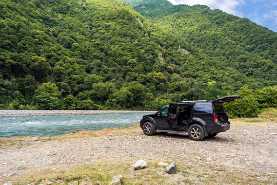 Road trip by car. A car standing near the river on a pebble rocks in the mountains. Wild nature background.