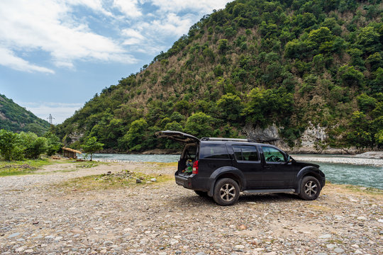 Road trip by car. A car standing near the river on a pebble rocks in the mountains. Wild nature background.