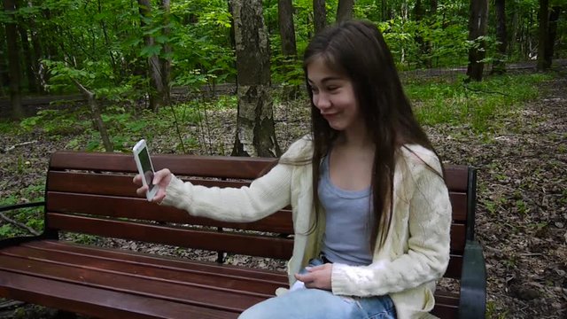 Girl taking selfie photo smartphone , loseup taking at park in summer. Posing and smiling. Video shooting static camera.
