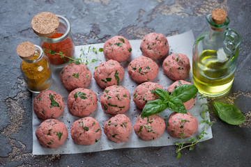 Fresh uncooked meatballs with seasonings and olive oil on a brown stone background, studio shot