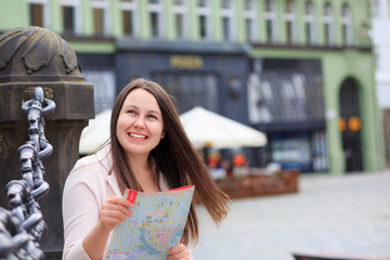 Pretty young brunette female tourist with a map discovering history foreign city, looking to...