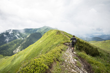 Fototapeta na wymiar man with hiking poles walking alone on high mountain ridge after summer storm
