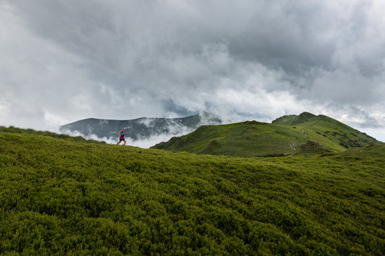 woman running alone outdoors in the summer storm over cloudy mountains trail