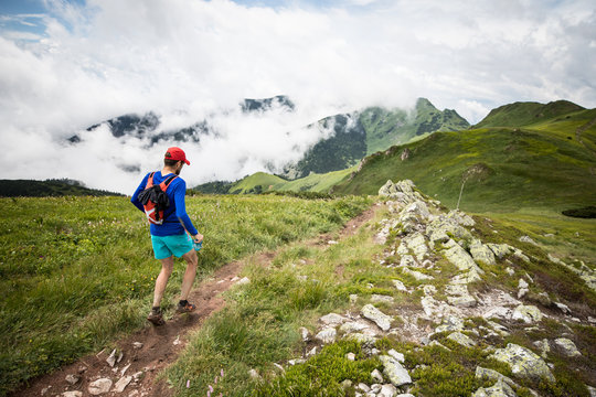 man running on natural high mountain trail with beautiful view at peaks and clouds