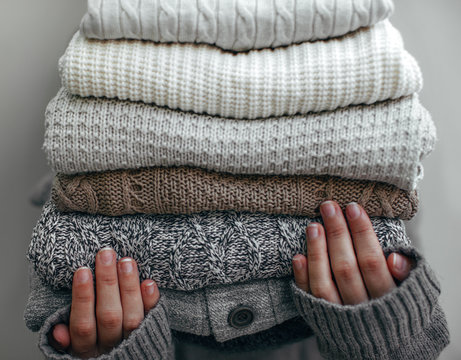 Woman holding a stack of winter wool sweaters.