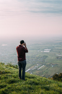 Young man standing on a cliff and photographing landscape