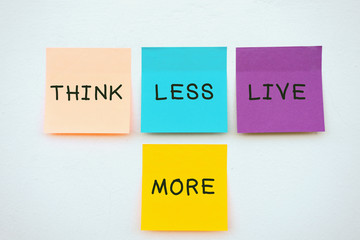 Think less live more - Inspirational and motivation quotes on colorful sticky paper on a wall, pastel colors.