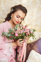 Beautiful young Bride with dark hairs sits on a sofa in a bedroom. Bride's morning.