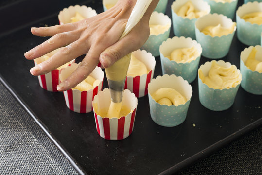Young woman hands piping cake mixture into molds for making muffin.