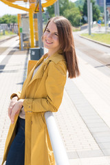 Young woman in a yellow raincoat waiting for a train at a railway station