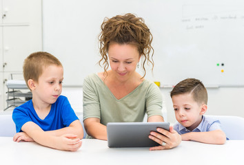 teacher woman using tablet computer with two preschooler boy in a classroom