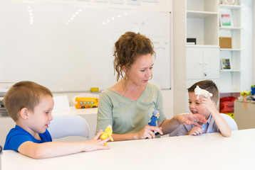 teacher woman playing with two child boy with finger puppets in the classroom
