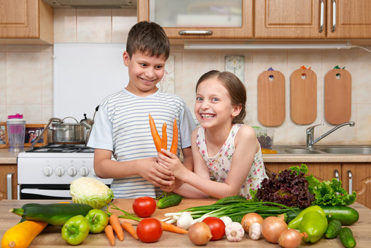 Child girl and boy having fun with tomatoes and carrot. Home kitchen interior with fruits and vegetables. Healthy food concept