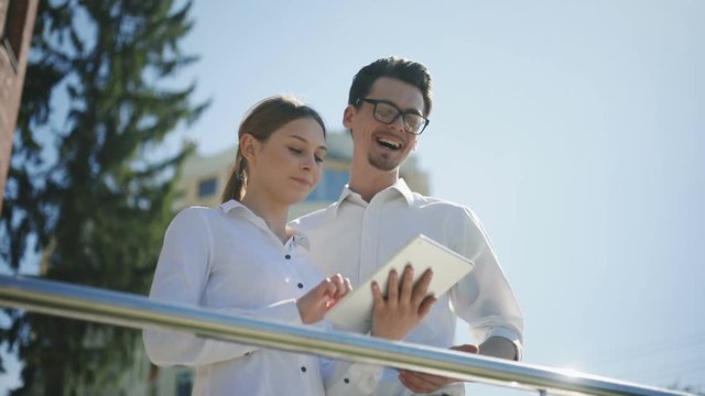 Young man woman using tablet computer standing public space talking laptop tapping touching screen speaking showing smiling glasses pair work laughing expression surprised emotional face summer