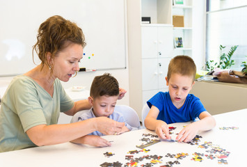 Fototapeta premium teacher woman and two preschooler boy playing with puzzle game in the classroom