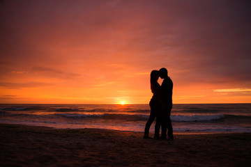 Obraz premium Couple in love having romantic tender moments at sunset. Honeymoon lovers hugging on beach. Silhouettes of couple against the sunset sky.
