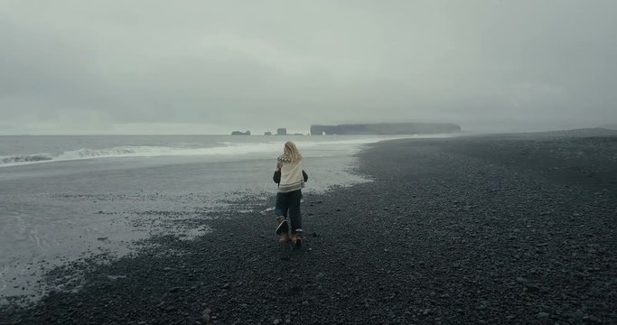 Aerial view of the young couple walking on the black volcanic beach in Iceland. Woman in lopapeysa jumps on the man arms