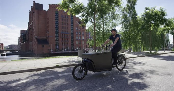 Handsome cargo bike courier is cycling on a street