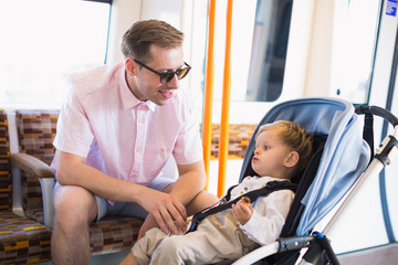 The little cute boy sits in pram in a bus near his happy father