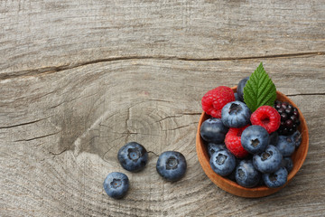 mix of blueberries, blackberries, raspberries in wooden bowl on old wooden table background. top view with copy space