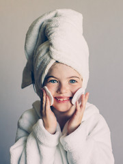 Funny little smiling girl with a mask for skin face and with a towel on her head, portrait on a...