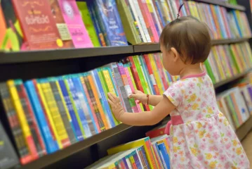 Stickers pour porte Garderie La petite fille asiatique choisit un livre dans la bibliothèque. Un enfant regarde les livres de la bibliothèque et décide lequel emporter chez lui. Créativité et imagination des enfants.