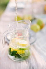food, healthlife, country, lifestyle, table setting concept - close-up of transparent jug with slices of lemon and leaves of mint and water running