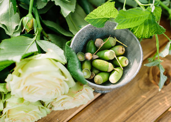 bouquet, flower, gift and floral arrangement concept - close up on fresh flowers and buds of white roses on a wooden table, a bowl with green acorns, leaves and flower buds with drops of dew