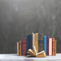 set of old books with open one on white wooden desktop with copy space on blackboard