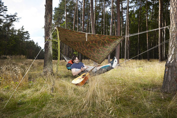 Obraz na płótnie Canvas Man in wild forest relaxing with guitar in hammock bed