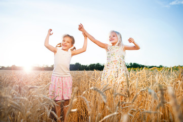 two little girls jumping at wheat field
