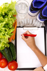 Healthy lifestyle concept. Writing weight loss plan with fresh vegetable diet and fitness