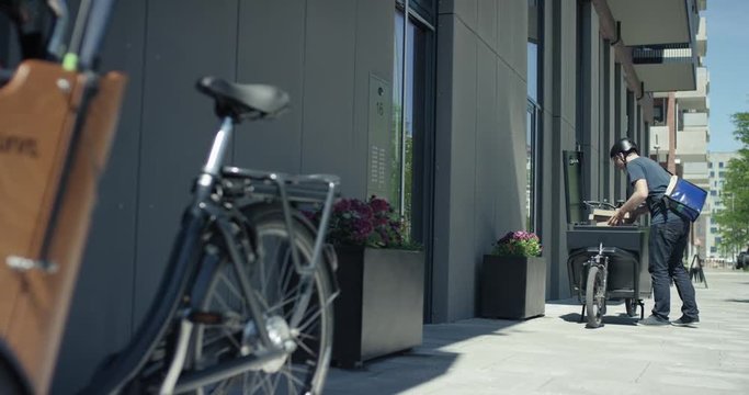 Handsome courier delivering packages to customers with his cargo bike