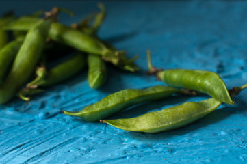 Young organic green pea pods and peas over blue texture background. Close up. Harvest, healthy eating.