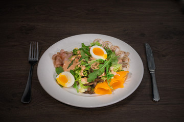 Salad with egg and mushrooms on a white plate and a wooden background