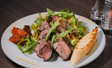Roasted meat with blood in a cut with vegetables on a wooden background